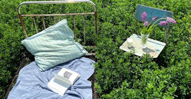 Open Concept - Bed with book near chair with flower bunch in field