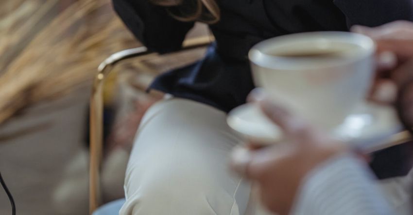 Coffee Podcasts - Crop anonymous female host talking to guest and having coffee while recording conversation on microphone