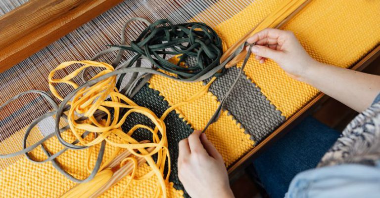 Durable Materials - Top view of crop anonymous female employee working on wooden weaving loom machine with stretched durable colorful threads in workshop